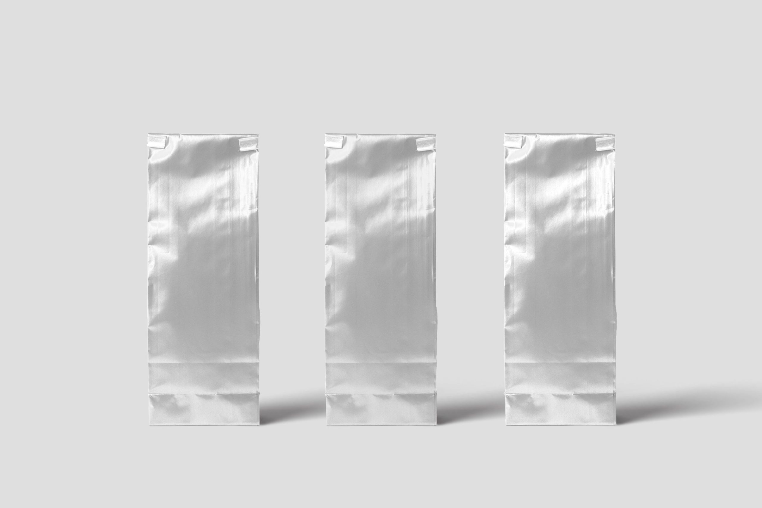 custom-mylar-stand-up-pouches Three shiny silver custom Mylar stand-up pouches displayed on a clean light background