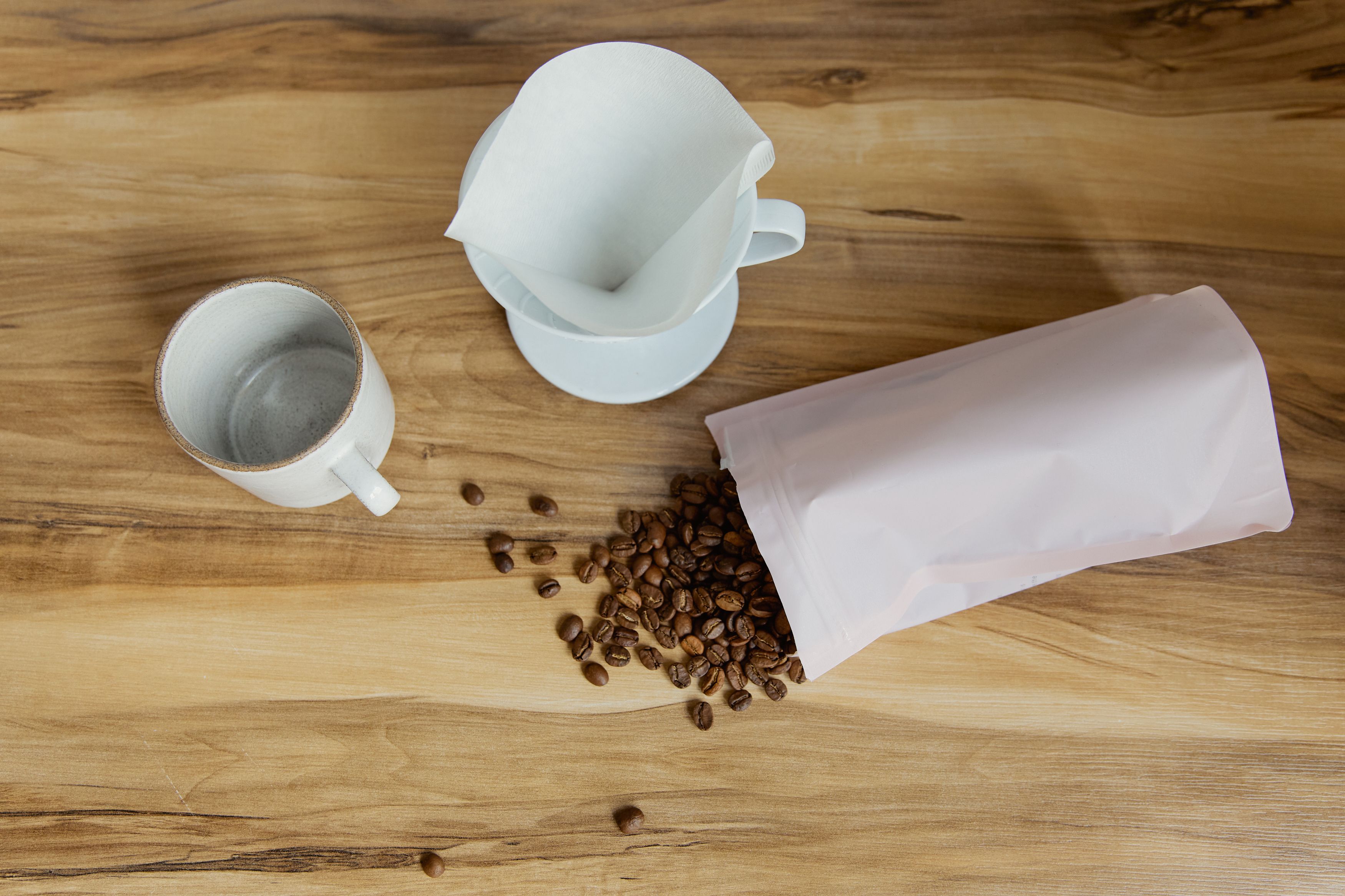 Stand-up Mylar pouch filled with coffee beans beside a cup on a wooden table